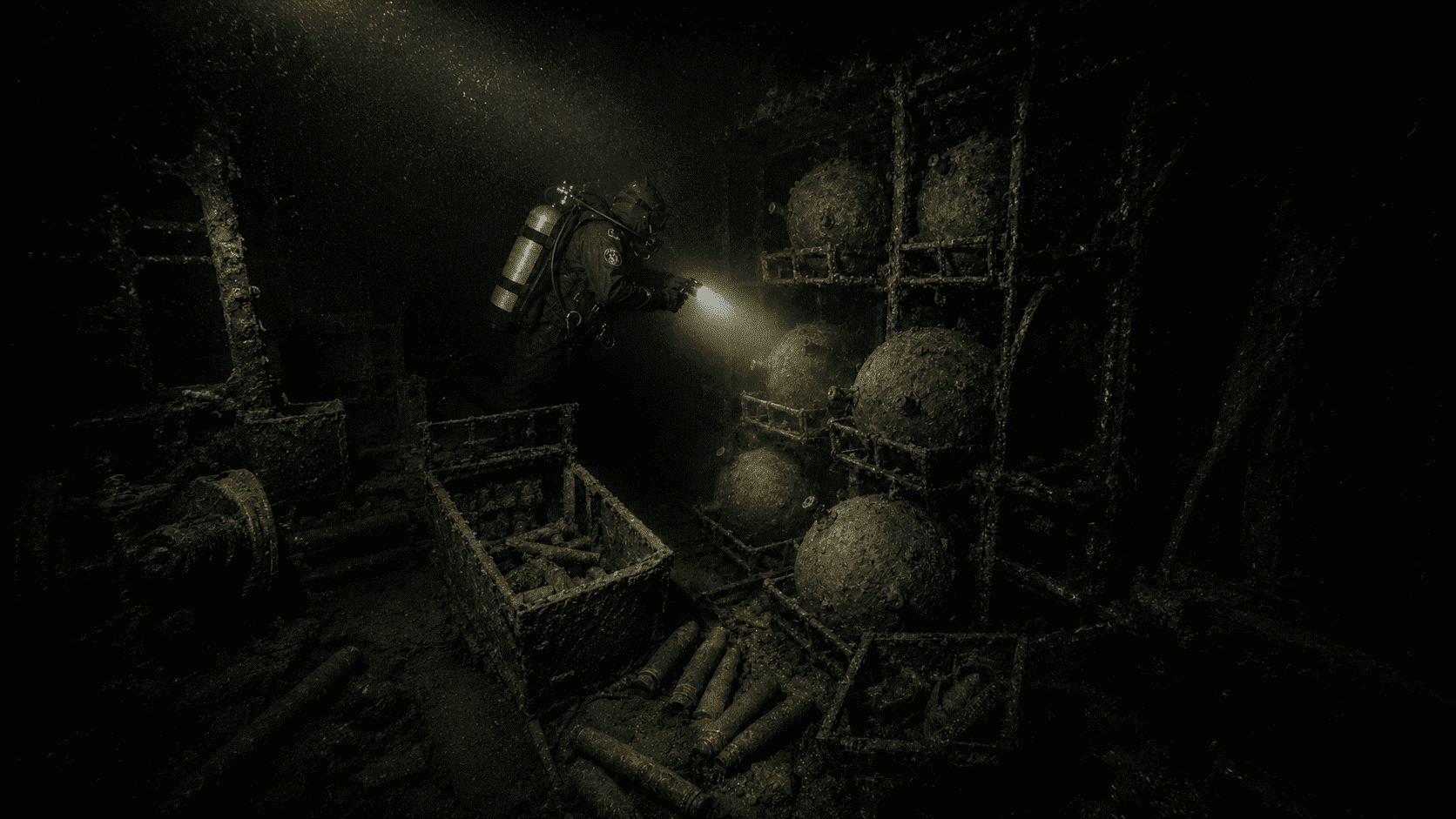 Diver illuminating stacked corroded sea mines and artillery shells inside the sunken warship